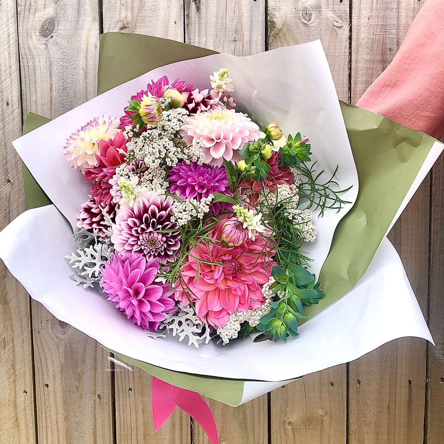 Bouquet of flowers wrapped in paper with a pink ribbon against a wooden background